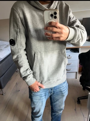 Grå CP Company hoodie  - Helt ny CP Company hoodie, modellen i bilden är 173 cm och väger 64 kg. Passar någon som är runt 180 cm lång. Hör gärna av er vid funderingar