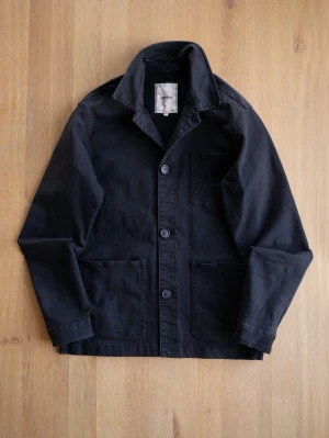 Svart overshirt med tre fickor från Produkt.  - Stilren svart overshirt i kraftigt bomullstyg med tre utanpåliggande fickor och knäppning framtill. Klassisk krage och raka ärmar ger en avslappnad look. Perfekt att bära över en t-shirt för en enkel men snygg stil.
