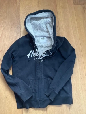 Svart Hollister hoodie med dragkedja - Svart/ väldigt mörk blå zip hoodie av Hollister. Säljer eftersom den var kvinno modell. Den borde passa dig som grabb om du är lite mindre än S. 