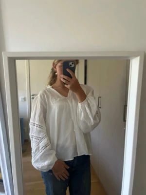 Vit blus med spetsdetaljer - Säljer en luftig vit blus med v-ringning och fina spetsdetaljer på ärmarna. Blusen har ballongärmar och knappar framtill. Perfekt till jeans eller kjol för en fräsch och enkel look. Passar S/M☺️