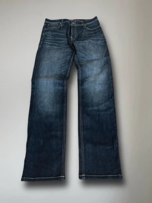 Mörkblå bootcut jeans  - Säljer ett par mörkblå bootcut jeans från Jack & Jones. Jeansen har en lätt tvättad look och raka ben med något utsvängd passform. Perfekta för en avslappnad och trendig stil. Måtten är: bredd: 43, längd: 102.