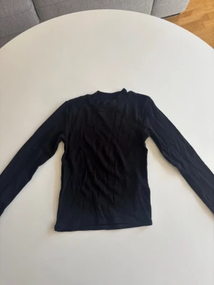 Svart långärmad polotröja - En enkel svart långärmad polotröja i mjukt och stretchigt material. Tröjan har en högre krage och smal passform, perfekt att styla lager på lager eller bära som den är. Klassisk och tidlös design som funkar till mycket.