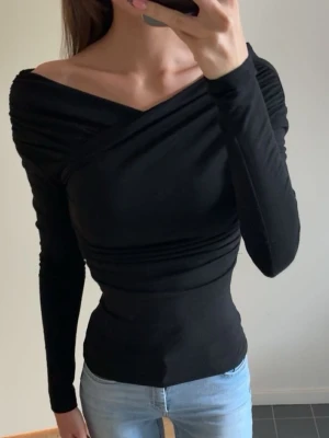 Svart omlottopp med lång ärm - Svart omlottopp med lång ärm och offshoulder-design från Zara. Toppen har åtsittande passform och rynkade detaljer längs axlar och midja. Läs min bio för mer info! 