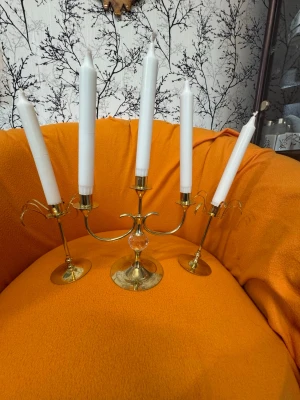 Guldfärgade ljusstakar i metall - Säljer tre eleganta ljusstakar i guldfärgad metall, varav en är en trearmad kandelaber och två är enkla ljusstakar. Alla har plats för höga stearinljus och har en klassisk, stilren design som passar perfekt som dekoration i hemmet.
