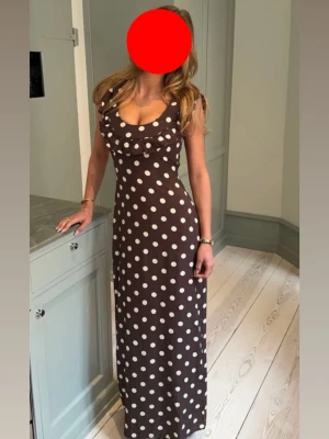 Brun prickig långklänning med volang från design by si - Snygg brun långklänning med vita prickar och volangdetalj vid urringningen. Använd nån gång