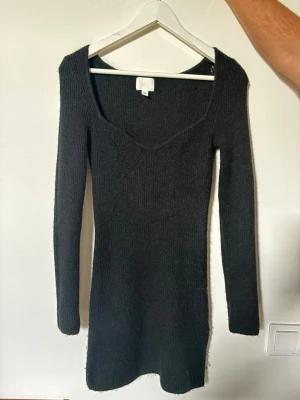 Svart ribbad stickad klänning - Mysig svart stickad klänning med ribbad struktur och lång ärm. Klänningen har en djup v-ringning och är figurnära i modellen, perfekt för dig som gillar en enkel men snygg look.