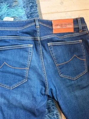 Jacob Cohën jeans NICK - Säljer ett par klassiska blå jeans från Jacob Cohën Milano. Jeansen har raka ben, två bakfickor med dekorativa sömmar och en brun läderpatch med logga bak i midjan. Snygga kontrastsömmar och tidlös design. W33 L33