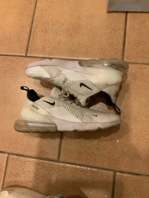 Vita Nike Air Max 270 sneakers - Säljer ett par vita Nike Air Max 270 sneakers med transparent sula och svarta detaljer. Skorna har en sportig design med mesh-överdel och synlig Air-enhet i hälen. Perfekta för dig som gillar streetwear och vill ha bekväma sneakers med modern look. Även sköna att springa och sporta i och allmänt perfekta för vardagen.⭐️