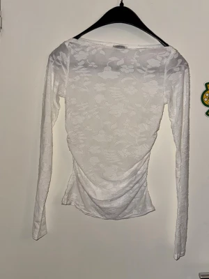 Vit blommig långärmad topp - Säljer en vit långärmad topp med blommigt mönster i transparent mesh. Toppen har en figurnära passform och lätt drapering baktill. Perfekt för dig som gillar stilrena men ändå unika plagg.