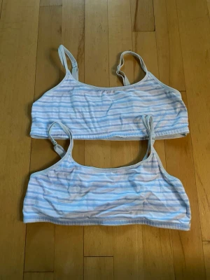 Två randiga bralettes i pastell - Säljer två mjuka bralettes med tunna axelband och pastellfärgade ränder i blått och vitt. De har en enkel, sportig design utan vaddering och är perfekta för en avslappnad look. Materialet känns stretchigt och bekvämt mot huden.
