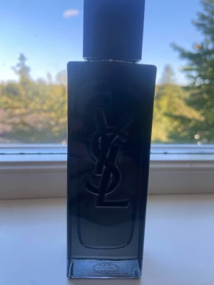 Mörkblå parfymflaska från YSL - Säljer en stilren parfymflaska från YSL i mörkblått glas med den klassiska YSL-loggan i relief på framsidan. Flaskan har en fyrkantig form och svart lock, perfekt för dig som gillar exklusiva dofter och snygg design. Ny pris 1200 60ml ca 35-45 kvar 