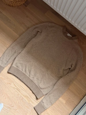 Beige stickad tröja These Glory Days - Snygg beige stickad tröja från These Glory Days. Tröjan har rund halsringning, ribbade muddar vid ärmslut och nederkant samt en grovstickad struktur med ett vitt mönster. Perfekt för dig som gillar en stilren och enkel men ändå unik look.