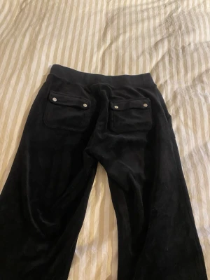 Svarta velourbyxor Juicy Couture - Säljer ett par svarta mjukisbyxor från Juicy Couture i mjuk velour. Byxorna har två fickor bak med knappar och bred resår i midjan.