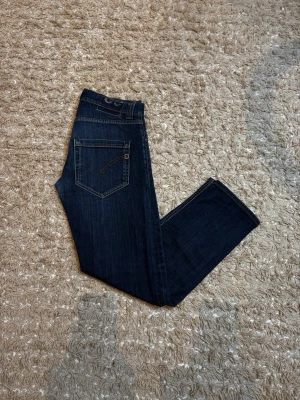 Dondup jeans - Säljer ett par mörkblå jeans med rak passform och snygg dragkedjedetalj på bakfickan. Jeansen har klassiska fickor och kontrastsömmar. Perfekta till en avslappnad streetstil eller att matcha med en hoodie.