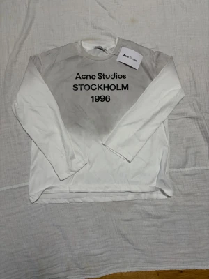 Vit långärmad topp Acne Studios - Säljer en vit långärmad topp från Acne Studios med trycket 'STOCKHOLM 1996' på bröstet. Klassisk rund halsringning och avslappnad passform. Perfekt för dig som gillar minimalistisk och stilren design.