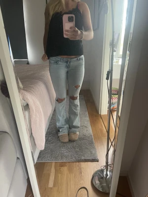 Ljusblå slitna raka jeans - Säljer ett par ljusblå jeans med raka ben och stora slitningar vid knäna. Jeansen har klassisk femficksmodell och är tillverkade i denim. Perfekta för en avslappnad och trendig look.