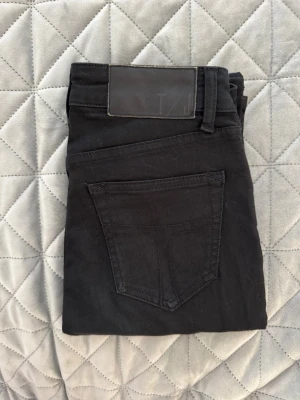 Tiger of Sweden - Svarta slim fit jeans - Snygga svarta slim fit jeans med klassisk femficksdesign och bälteshällor. Jeansen har en stilren look och är tillverkade i ett mjukt denimtyg som ger en bekväm känsla. Perfekta för dig som gillar en enkel och clean stil.