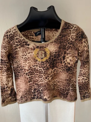 Leopardmönstrad topp med brodyr - Cool topp med leopardmönster i bruna toner och guldfärgad brodyr med bokstaven G framtill. Rund halsringning och trekvartsärm. Perfekt för dig som vill sticka ut lite extra.0377