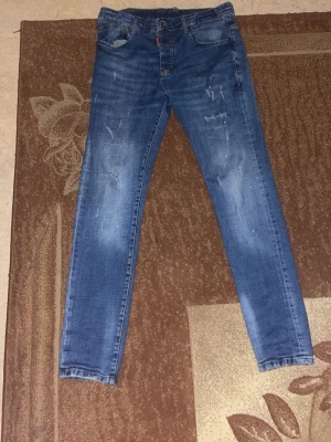 Blå slitna skinny jeans - Säljer ett par blå skinny jeans med slitningar och lätt tvättade detaljer. Jeansen har klassisk femficksmodell och dragkedja med knapp. Perfekta för en avslappnad och trendig look.