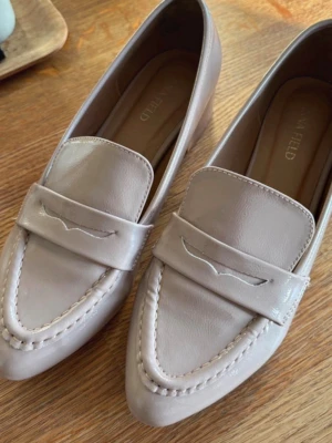 Puderrosa loafers från Anna Field - Snygga puderrosa loafers från Anna Field i glansigt konstläder. Skorna har en klassisk penny loafer-design med dekorativ söm och markerad rem över foten. Perfekta för dig som gillar stilrena och tidlösa skor med en modern touch. Använda en gång (se undersidan) samt kom med ett knappt synligt streck (se bild) som defekt vid köp.