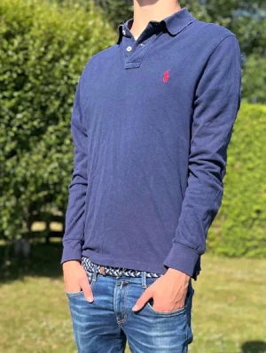 Polo Ralph Lauren Pike - Säljer en marinblå långärmad pike med röd broderad logga på bröstet från Polo Ralph Lauren i slim fit passform. Den är i M men sitter som S! Priset är ej hugget i sten, hör av dig vid minsta fråga.