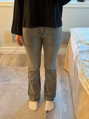 Grå bootcut jeans med hög midja - Säljer ett par gråa jeans med bootcut-modell och hög midja. Jeansen har klassisk femficksdesign och stängs med dragkedja och knapp. passformen är figurnära upptill med utsvängda ben.