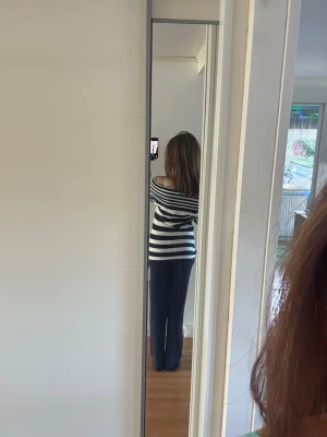 Randig stickad tröja med båtringning - Säljer en stickad tröja med breda marinblå och vita ränder. Tröjan har en avslappnad passform, lång ärm och båtringad hals som kan bäras off-shoulder. Materialet ser mjukt och bekvämt ut, perfekt för en chill look. Liten fläck se bild men jag tror den går bort i tvätten 