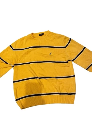 Gul stickad tröja från Nautica - Gul stickad tröja från Nautica med svarta och vita horisontella ränder. Tröjan har rund halsringning och en liten broderad logga på bröstet. Perfekt för dig som gillar färg och klassisk stil.