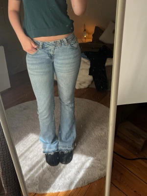 Ljusblå bootcut jeans med låg midja - Säljer ett par ljusblå bootcut jeans med låg midja och klassisk femficksmodell. Jeansen har slitna detaljer vid bensluten och är tillverkade i denim med lätt stretch. Perfekta för en avslappnad och trendig look.