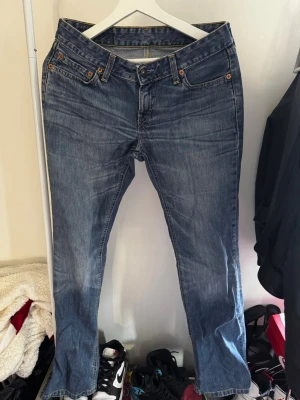 Blå Levi's bootcut jeans - Säljer ett par klassiska blå Levi's jeans med bootcut passform, och i low-waist. Jeansen har fem fickor, orangea sömmar och en snygg tvättad look. Levi's patch bak i midjan och röda detaljer på bakfickan. Perfekta för dig i storlek 36, och längden är lite lång på mig(är 163cm)