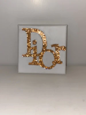 Canvas med texten 'Dior'  - En egen gjord bedazzlad tavla med motiv av loggan 'Dior'. Den är i en champagne/guldfärg. Canvasen är måtten 12x12cm.                                     Pris kan diskuteras