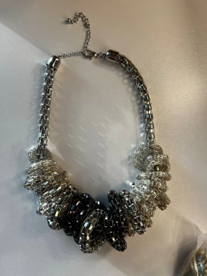 Chunky halsband i silver och svart - Säljer ett statement halsband med stora, glittriga länkar i silver och svart. Halsbandet har en robust kedja och flera ringformade detaljer som ger en cool och modern look. Perfekt för dig som vill sticka ut med accessoarerna.