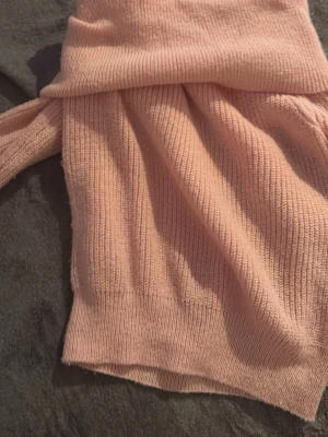 Ljusrosa stickad polotröja - Mysig ljusrosa stickad polotröja med bred polokrage och ribbade muddar. Tröjan har lång ärm och är tillverkad i ett mjukt, stretchigt material som känns skönt mot huden. Perfekt för kyliga dagar och enkel att matcha med jeans eller kjol.