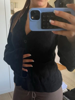 Svart kofta från arket - Mysig svart kofta med v-ringning och stora knappar framtill. Koftan har två fickor och ribbade muddar vid ärmslut och nederkant. Perfekt för lager på lager och enkel att matcha med olika outfits.