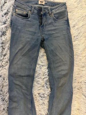 Ljusblå low boot jeans från 157 - Säljer ett par ljusblå jeans från 157 med klassisk femficksmodell och raka ben. Jeansen har bälteshällor, knappgylf och är tillverkade i ett mjukt denimtyg. Perfekta för en avslappnad och trendig look.
