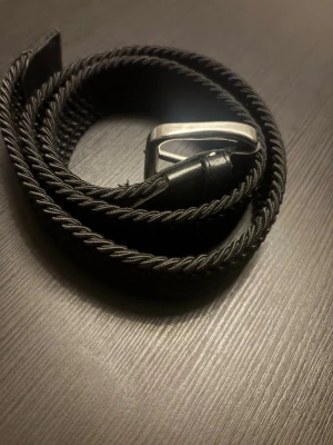 Svart flätat bälte med silverfärgat spänne - Snyggt svart flätat bälte med ett stilrent silverfärgat spänne. Aldrig använd och är i perfekt skick. Perfekt accessoar för att lyfta din outfit.