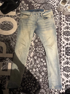 Ljusblå slim fit jeans från Diesel - Säljer ett par ljusblå slim fit jeans från Diesel med snyggt slitna detaljer och klassisk femficksdesign. Jeansen har en låg midja och smal passform, perfekt för en trendig och avslappnad stil. Materialet är mjukt denim som ger en skön känsla hela dagen.