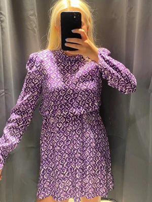 & Other stories Lila mönstrad långärmad klänning - Kort klänning i lila med vitt mönster. Klänningen har långa ärmar, hög hals och en lätt utställd kjol. Materialet känns mjukt och stretchigt, troligen polyester. Perfekt för dig som gillar färg och mönster.
