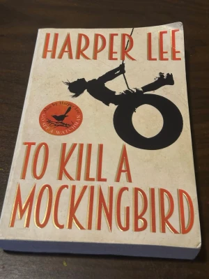 To Kill a Mockingbird av Harper Lee - En klassisk roman av Harper Lee med ett omslag i beige och svart, där en siluett av ett barn på ett bildäck syns. Boken utforskar teman som rasism och rättvisa i den amerikanska södern under 1930-talet. Perfekt för dig som gillar djupa och tankeväckande berättelser.