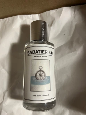 SABATIER 3.0 extrait de parfum - Säljer en SABATIER 3.0 extrait de parfum från one bold chemist. Flaskan är genomskinlig med en stilren silverfärgad kork och en etikett med en kompassillustration. Modern och minimalistisk design som passar perfekt i badrumshyllan.