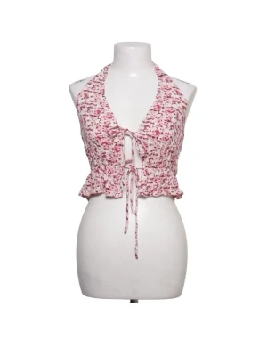 Rosa och vit blommig halterneck topp - Supersöt halterneck topp i vitt och rosa med blommigt mönster. Toppen har snörning framtill och volangkant nedtill. Perfekt för varma dagar och ger en riktigt somrig vibe.