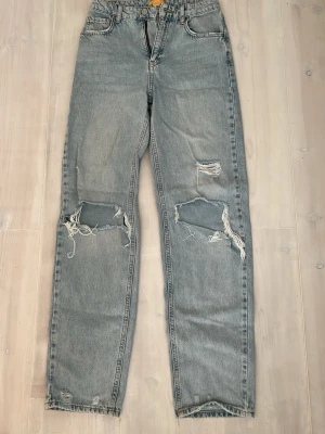 Ljusblå raka jeans med slitningar - Säljer ett par ljusblå jeans med raka ben och stora slitningar över knäna.