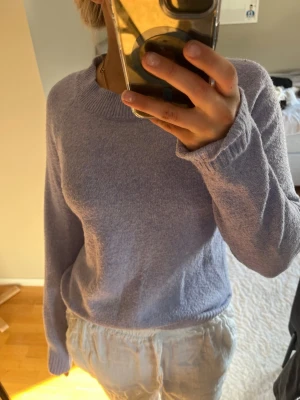 Ljuslila stickad tröja - Mysig ljuslila stickad tröja med rund halsringning och långa ärmar. Tröjan har en enkel, klassisk design med ribbstickade muddar vid halsen. Perfekt för dig som gillar en avslappnad och stilren look.