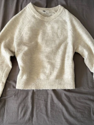 Beige stickad tröja - Mysig beige stickad tröja med och rund halsringning. Tröjan har långa ärmar och ribbade muddar vid ärmslut och nederkant. Perfekt för lager på lager och enkel att styla till olika outfits.