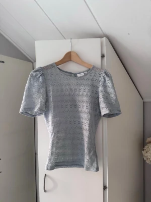 Ljusblå spetsblus med puffärm - Supersöt ljusblå topp med puffärmar och rund hals. Hela toppen är täckt av ett detaljerat spetsmönster som ger en romantisk vibe. Perfekt att styla med jeans eller kjol för en trendig look.