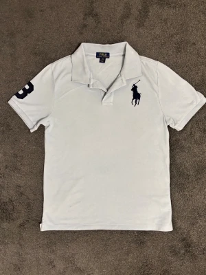 Vintage Ljusblå archive Ralph Lauren polo  - Säljer en riktigt fräsch och fin polo Ralph Lauren skjorta. Tröjan sitter som S/M men av nån anledning står de XL. Den är i fin ljusblå färg och nummer 3 på ärmen. Tröjan är vintage och hade de gamla märkena. Pytten liten fläck längst ner på tröjan som säkert går bort med medel eller tvätt.  Mått:  Bredd framifrån: ca 45-47cm  Längd framifrån: ca 65-67cm
