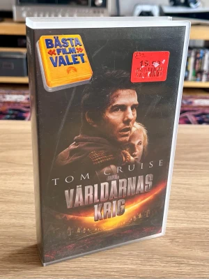 Världarnas krig (2005) – VHS – NY & INPLASTAD - Svensk VHS-utgåva av Steven Spielbergs Världarnas krig med Tom Cruise.  Kassetten är fortfarande fabriksinplastad och aldrig öppnad – ett riktigt fint exemplar för VHS-samlaren. 📼  Har dessutom kvar de ursprungliga butiksetiketterna på plasten, vilket ger den lite extra tidskapsel-känsla från VHS-erans sista år.  Skick: Ny / oöppnad / inplastad Format: VHS Svensk utgåva  Skickas väl emballerad.