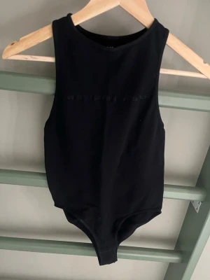 Svart body från Carin Wester - Snygg svart body från Carin Wester med diskret präglad logga framtill. Modellen har breda axelband och rund halsringning. Tillverkad i mjukt stretchigt material som sitter skönt mot kroppen. Perfekt att styla till jeans eller kjol.