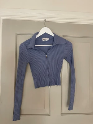 Blå ribbad ziptröja från NA-KD - Trendig blå ribbad ziptröja från NA-KD med lång ärm och krage. Tröjan har en croppad passform och dragkedja framtill. Perfekt att styla med jeans eller kjol för en cool look.