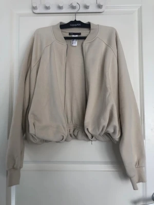 Beige sweatshirtjacka med dragkedja - Beige sweatshirt från Zara med dragkedja framtill och resår i midjan. Aldrig använd. Säljer den då jag ångrade mig efter att ha köpt den men inte hann lämna tillbaka.